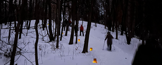 People snowshoeing with luminaries in the dark