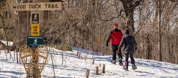 Two people snowshoeing past the wood duck trail sign