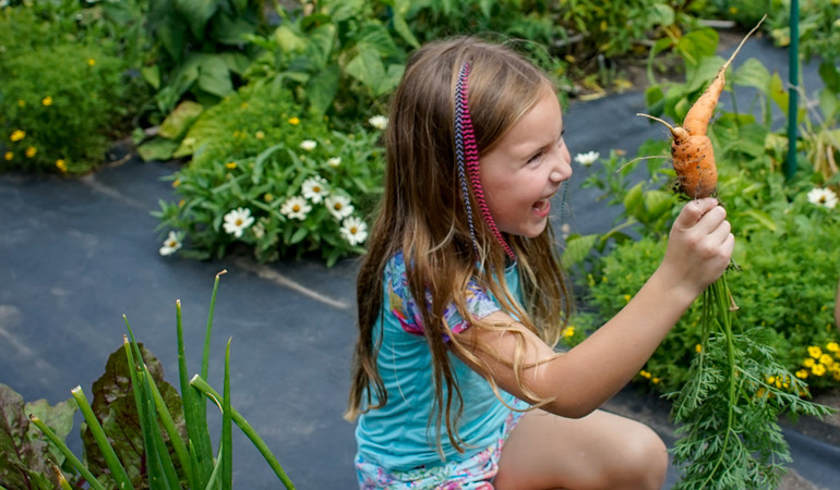 child holding carrot in the garden, photo by Jason Boudreau Landis