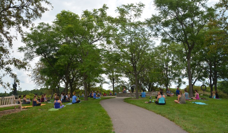 People seated in the grass along path in the garden for yoga class