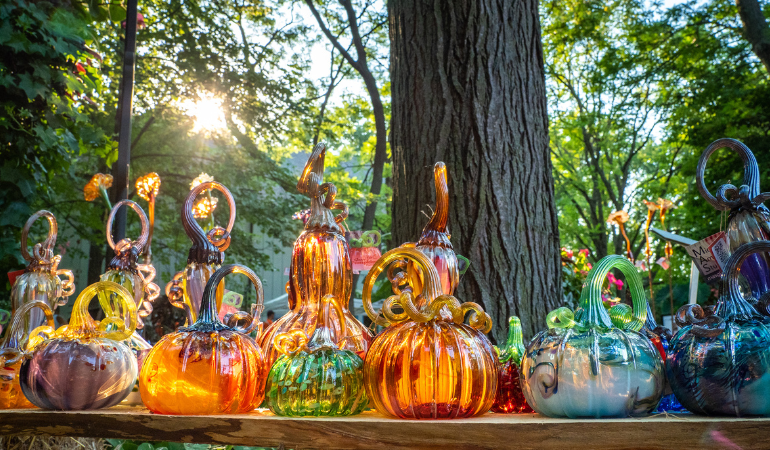 Glass pumpkins on a bench with a tree and sun behind