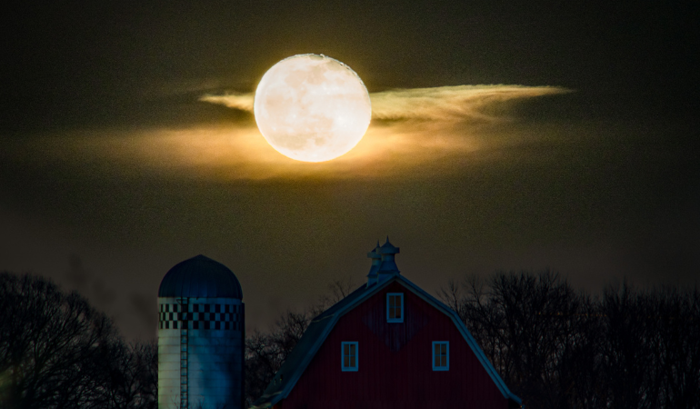 Yellow full moon over the barn at night