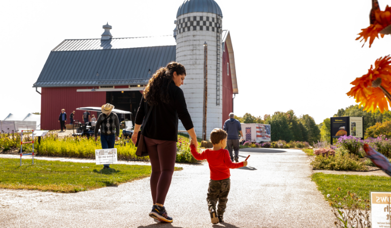 Mom and child holding hands walking towards the red barn